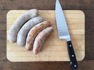 Parboiled sausage on cutting board with chef's knife.