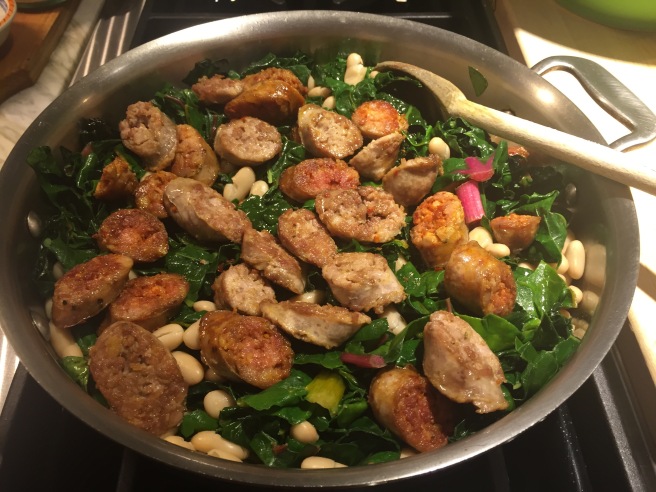 Adding sliced sausage to wilted greens and beans.