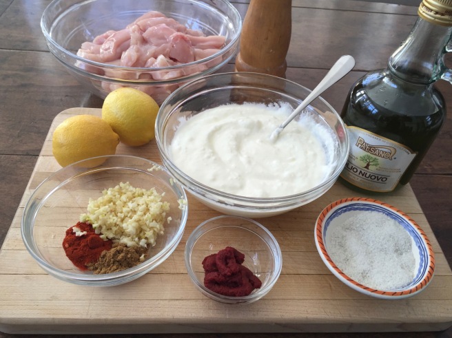 Shish Taouk ingredients on cutting board: ingredients: cubed chicken breast, plain yogurt, lemon juice, olive oil, garlic, smoked paprika, cumin, tomato paste, salt and pepper.